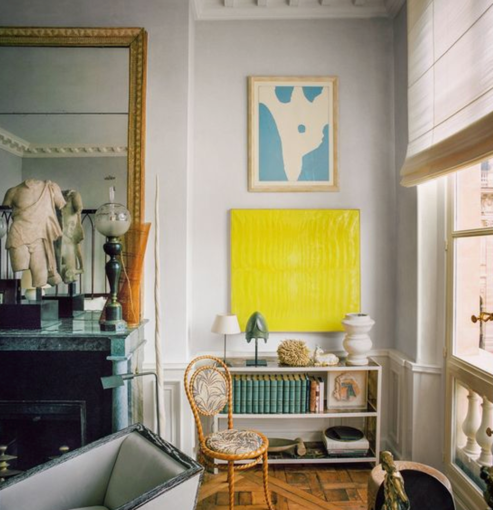 Gray walls with bright yellow piece of artwork on wall next to mantel and above short bookshelf