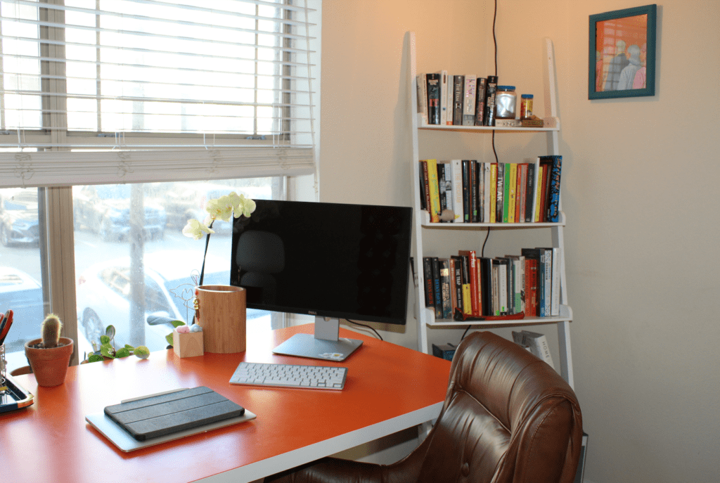 Bright orange desk against sunny window next to bookshelf in multipurpose office 