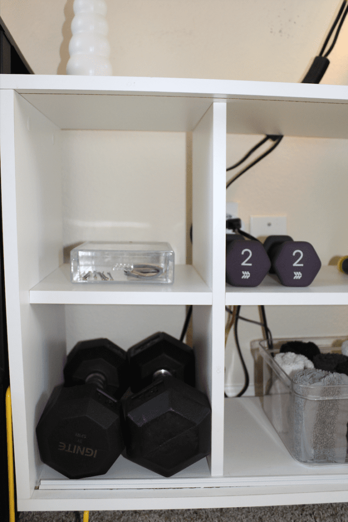shelf with free weights, rolled up towels, and an acrylic drawer with hair supplies