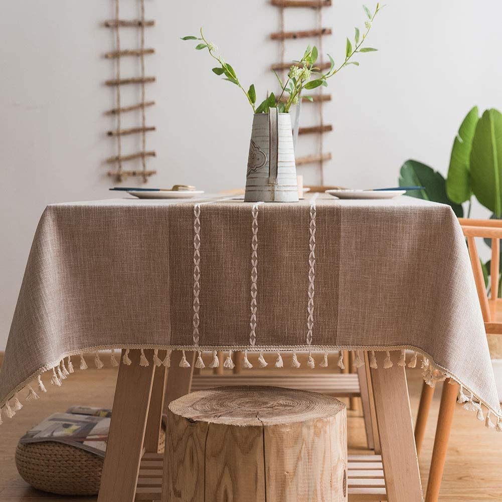 Embroidered oatmeal-colored tablecloth on a wooden dining table with wooden stool and bohemian details