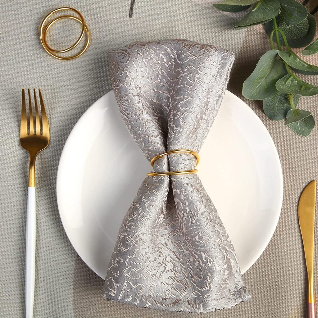 Gold spiral napkin rings on a silver textured dinner napkin with white and gold silverware