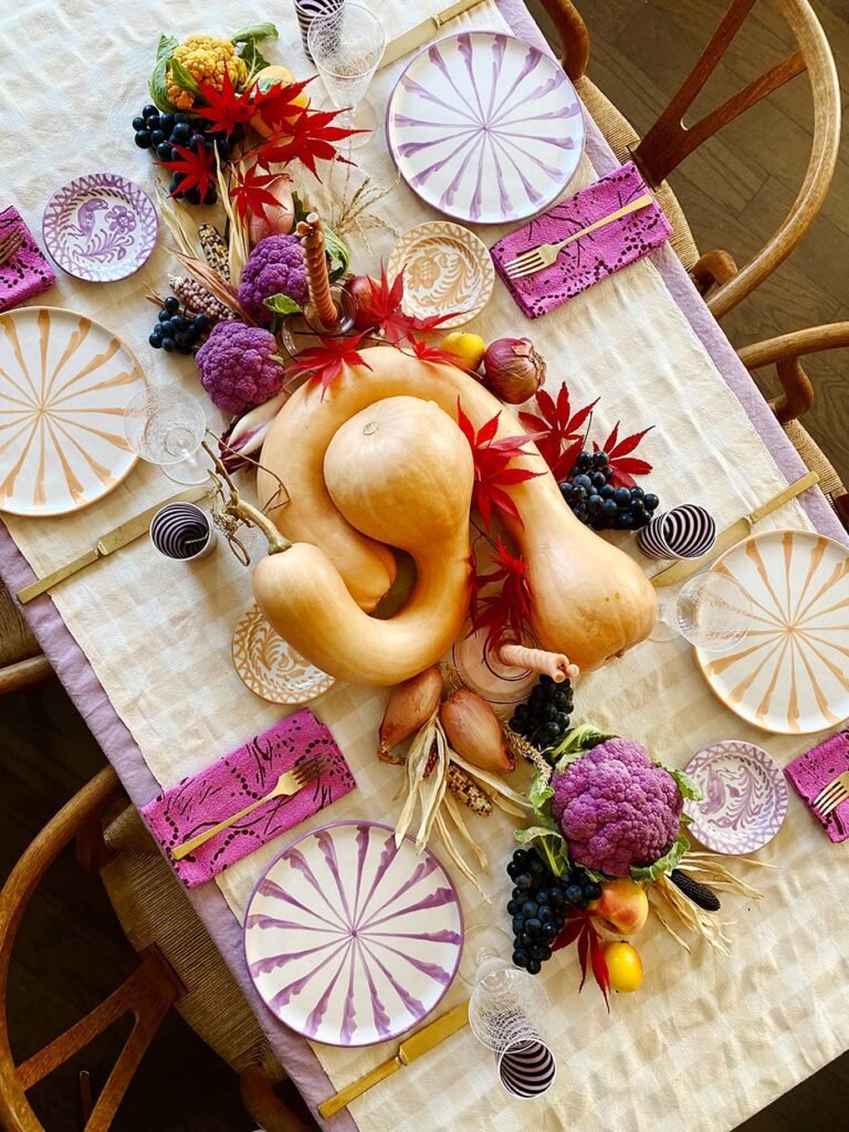 Domino pastel with pops of harvest hues unique thanksgiving tablescape with bright fuchsia napkins/plates, gold silverware, and gourds