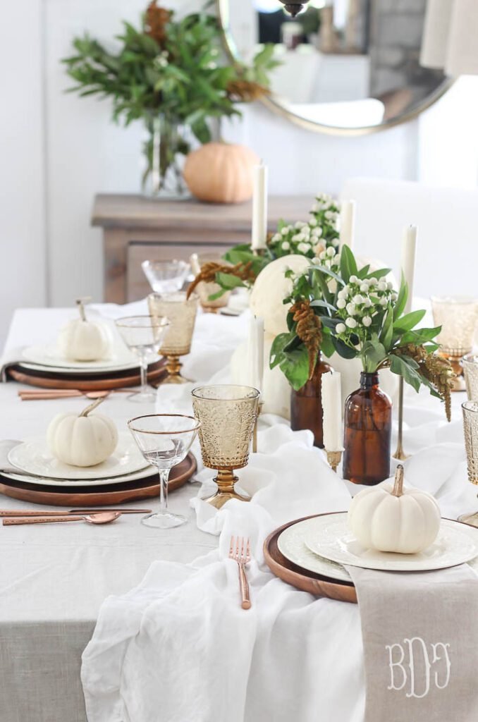 Rooms for rent traditional yet laid back thanksgiving tablescape with flowing white tablecloth, amber water glasses and apothecary jars, white pumpkins on each plate, and copper silverware/chargers