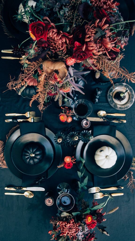 Jungalow wicked, thrifted, unique thanksgiving tablescape with black tablecloth, black plates, gold silverware and many rich, colorful accessories and plants