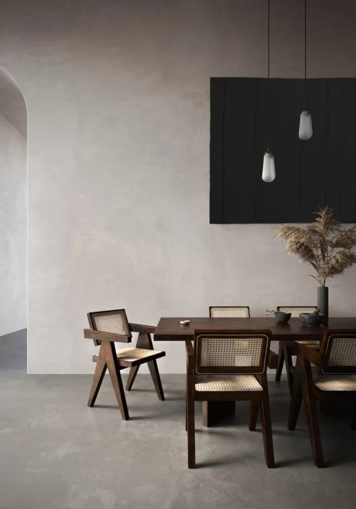 textural minimalism design in a dining room with concrete walls and flooring and rattan dining chairs