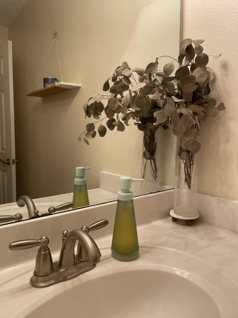 Sink with mint green soap dispenser and dried eucalyptus leaves in clear glass vase