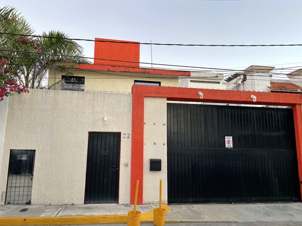 A two story house in Cancun with black doorways, cream-colored textured siding, and bright orange details