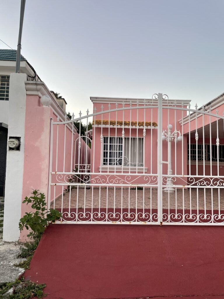 Bright pink house behind a intricately detailed white iron gate
