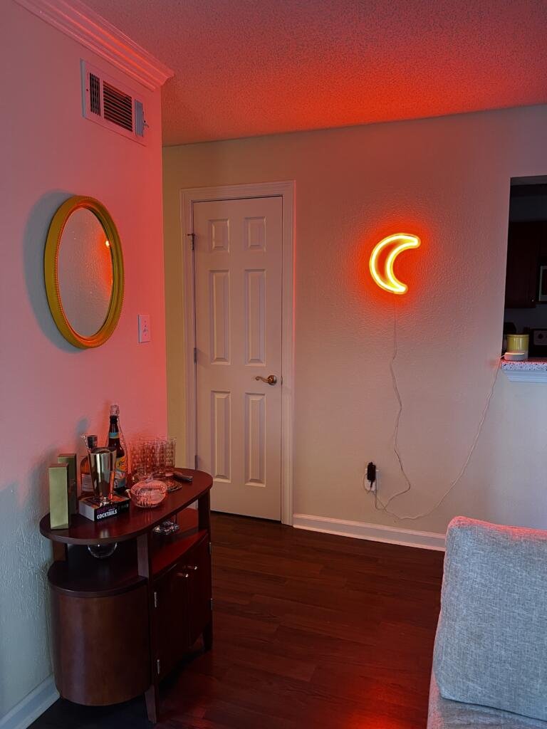 Living room with a dark wood bar cart next to an orange LED moon-shaped light fixture