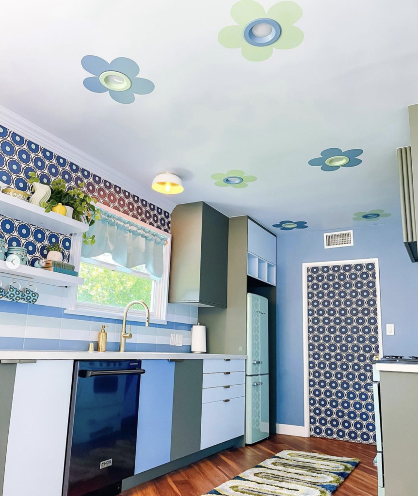 Fun blue kitchen with personality with multicolored cabinets, a fun graphic wallpaper and baby blue and green flowers painted around the flush light fixtures