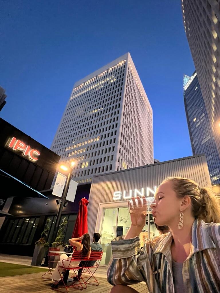 Hannah Michelle Lambert drinking champagne in the courtyard of Politan Row at Colony Square at night