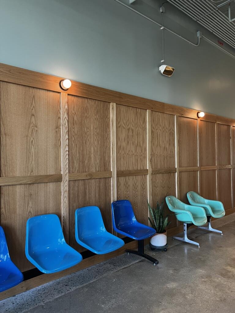 View of The Daily West Midtown wall with wood paneling on bottom half of the wall, light sage green on the top of the wall, and multi-colored blue-toned retro-style seating