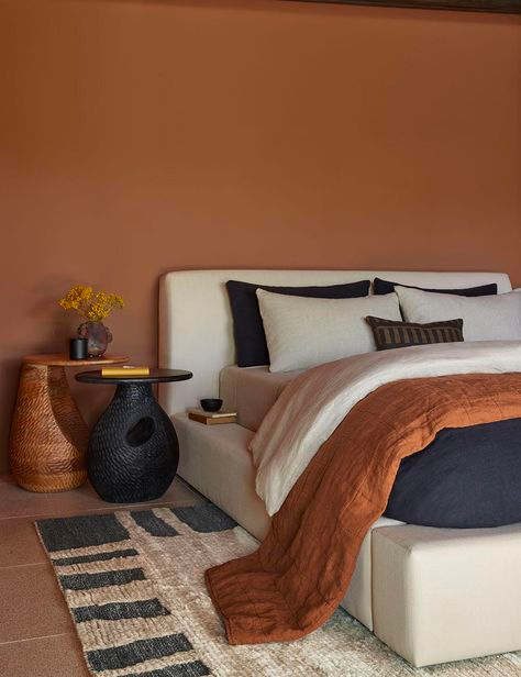 Luxurious bedroom with rust orange walls, a textural rug, organic shaped side tables and an upholstered bed frame