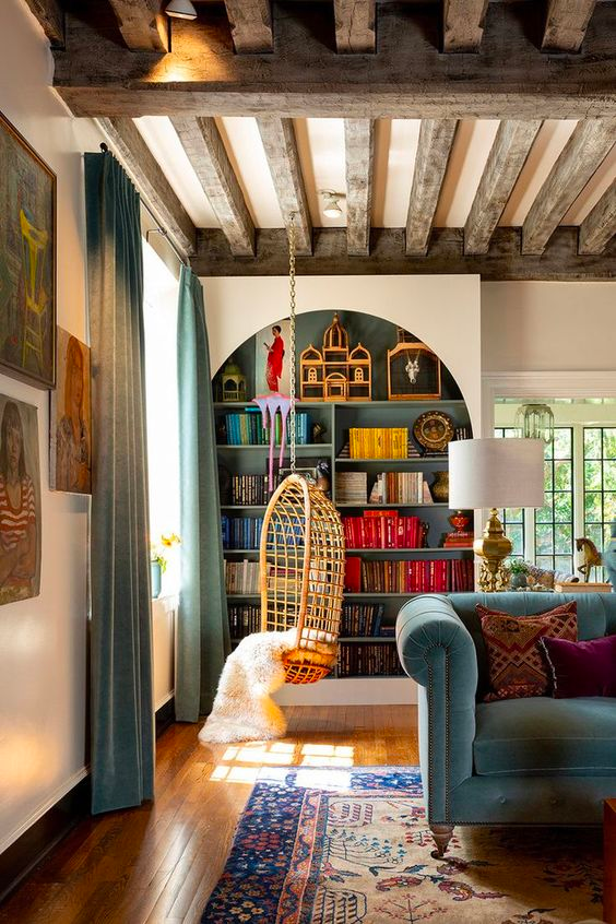 Comfortable and personable living room with a build in arched teal bookshelf, a swinging cane chair, a boho rug and a tufted light blue velvet sofa