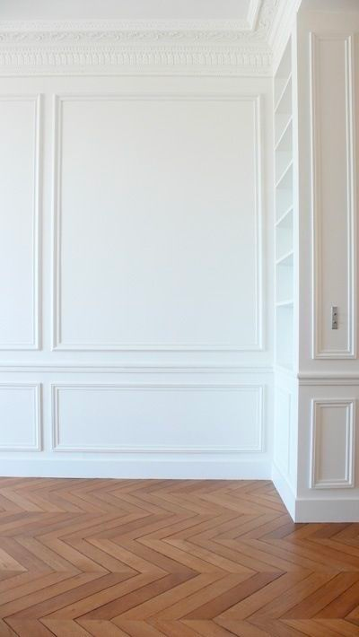 Empty room with warm herringbone floor and white walls with decorative molding
